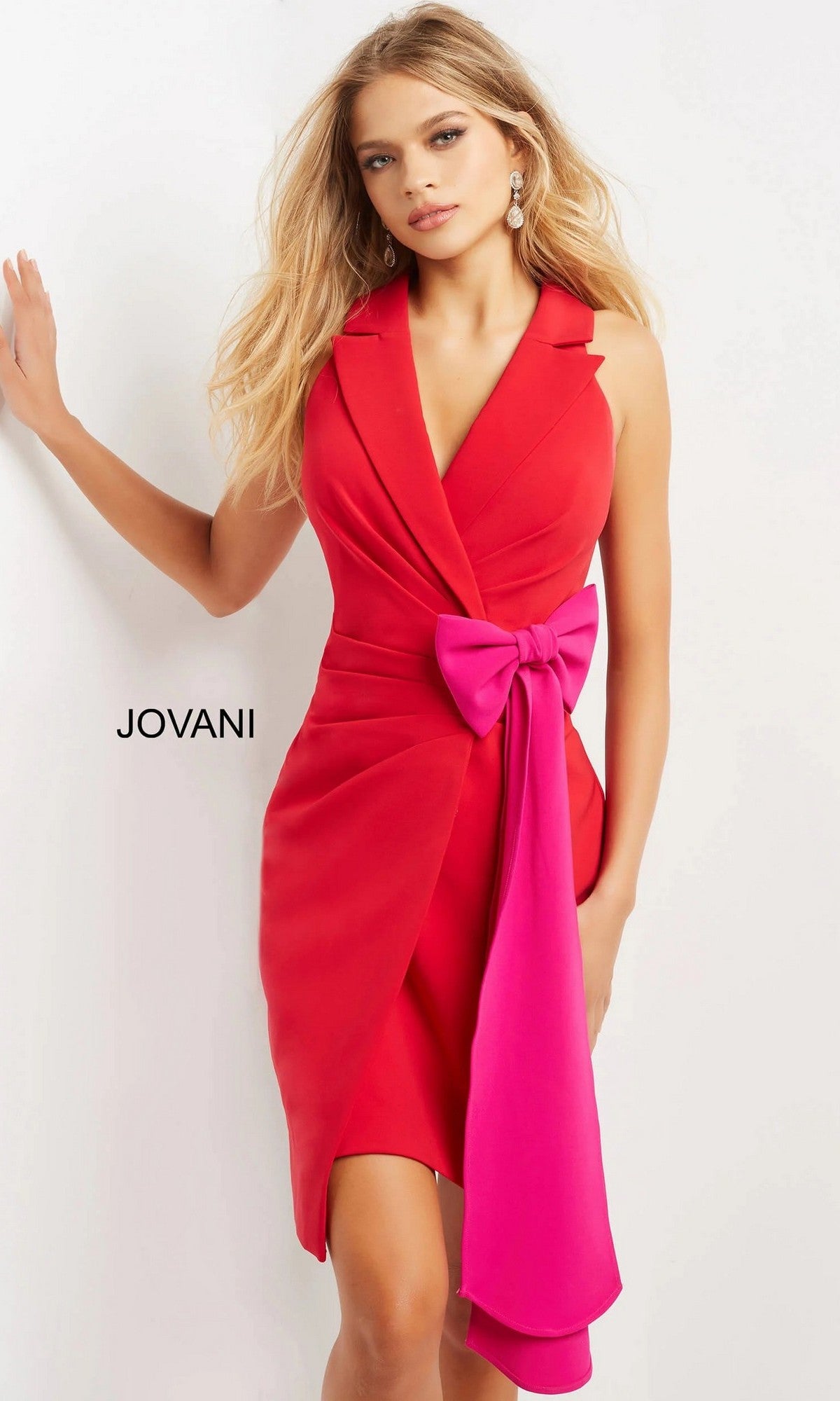 A woman wearing the Jovani 07961 Short Party Dress—a sleeveless red cocktail dress featuring a deep V-neck and a large pink bow at the waist—stands against a white background.